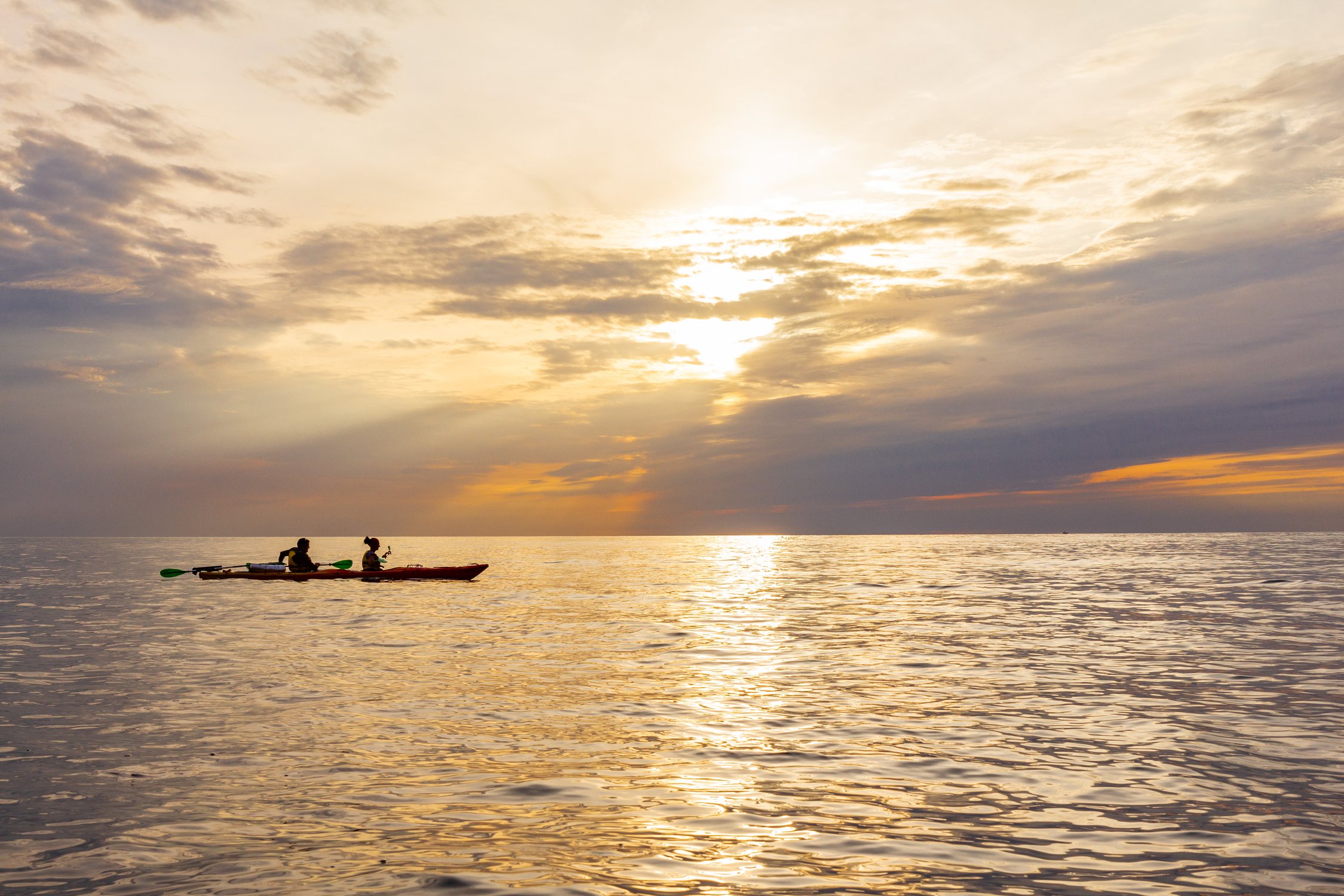 Два каякера плывут на каяке по черному морю вдоль берега  на фоне прекрасного заката.  Побережье Крыма.