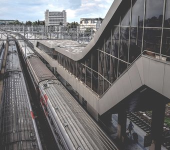 Железнодорожный вокзал в Адлере. На путях стоят пассажирские поезда, с платформ поднимаются пешеходные галереи в здание вокзала.