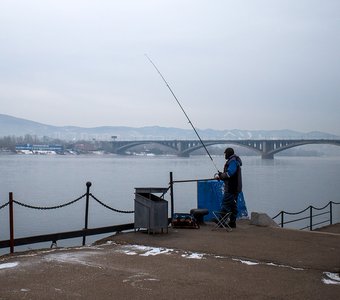Рыбак на Енисее в центре Красноярска. На фоне - Коммунальный мост, который изображен на десятирублевой купюре