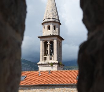 Вид на колокольню собора Святого Иоанна Крестителя в Будве через бойницу цитадели, Черногория