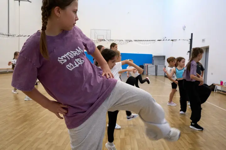 Девочка в фиолетовой футболке выполняет подъём колена, группа повторяет движение