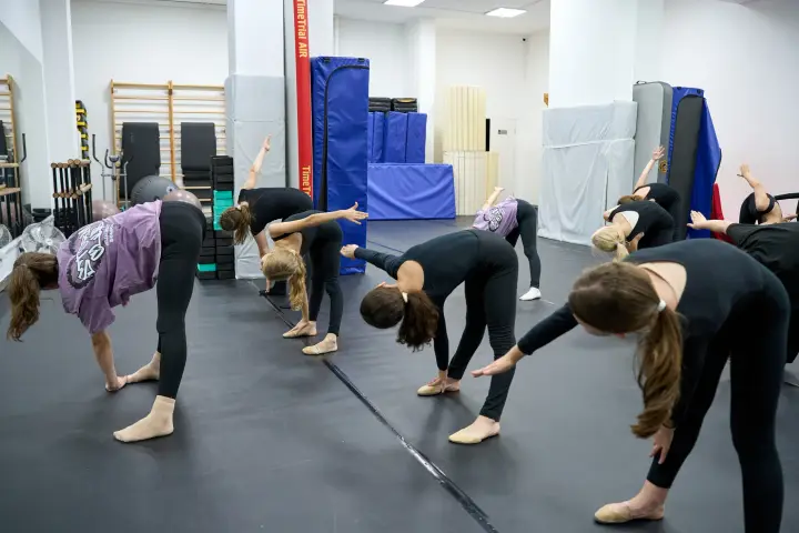 Спортсменки выполняют боковые наклоны на разминке в зале