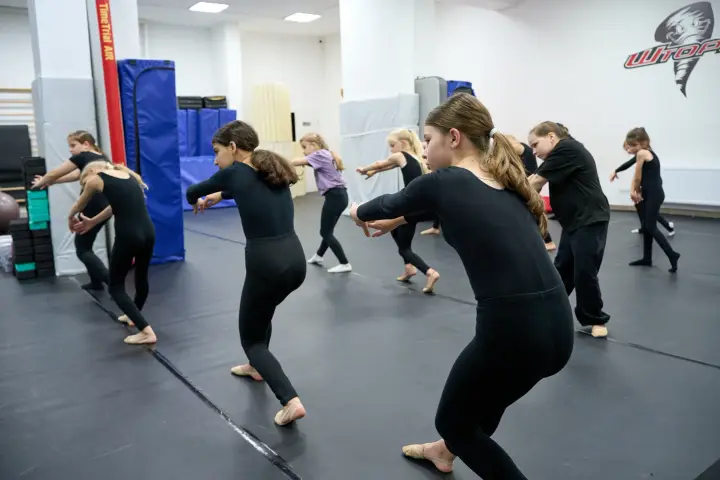 Группа спортсменок в чёрной форме выполняет разминку перед зеркалом