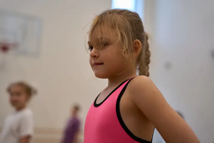 Юная спортсменка в розовом топе слушает объяснение на тренировке