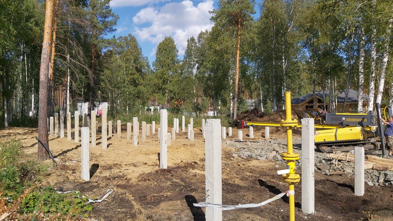 Свайное поле под дом; на переднем плане жёлтая стойка, справа видна свайно‑забивная установка