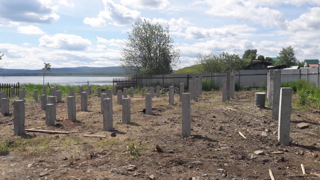 Свайное поле под коттедж; слева видна стрела автокрана, на заднем плане озеро и холмы.