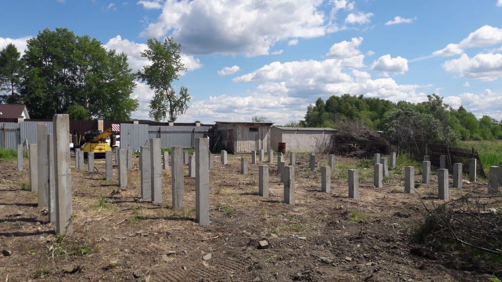 Свайное поле из железобетонных столбов на береговом участке; на заднем плане озеро, холмы и деревянный штакетник.