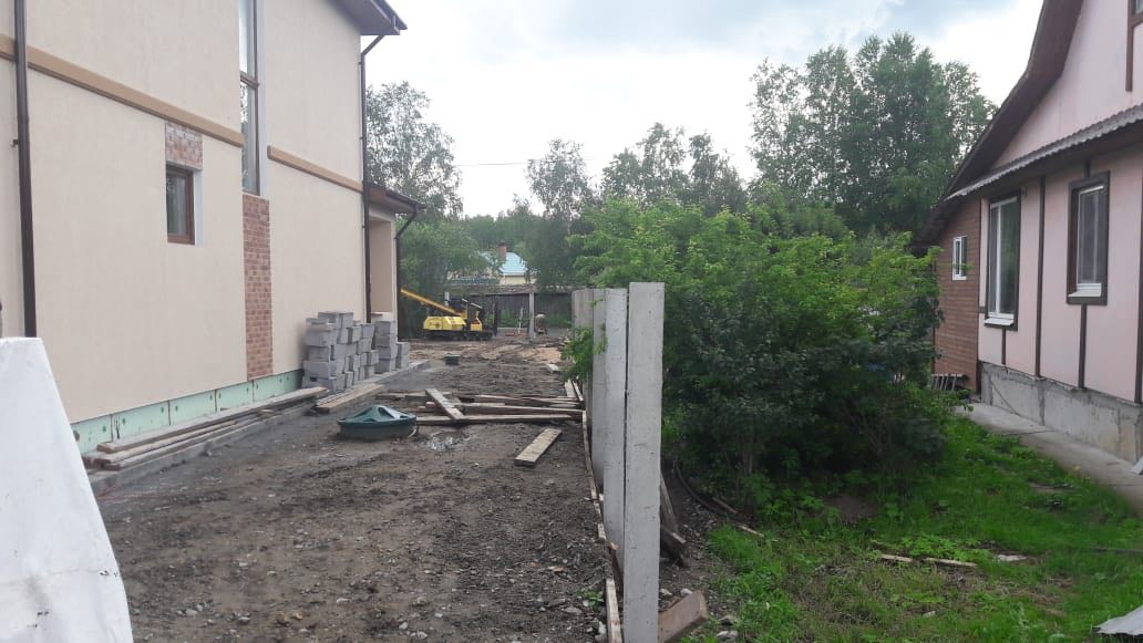 Ряд бетонных опор для будущего забора на участке, земляное основание и разбросанные доски; дом справа, зелень слева (Нижний Тагил, Черемушки)