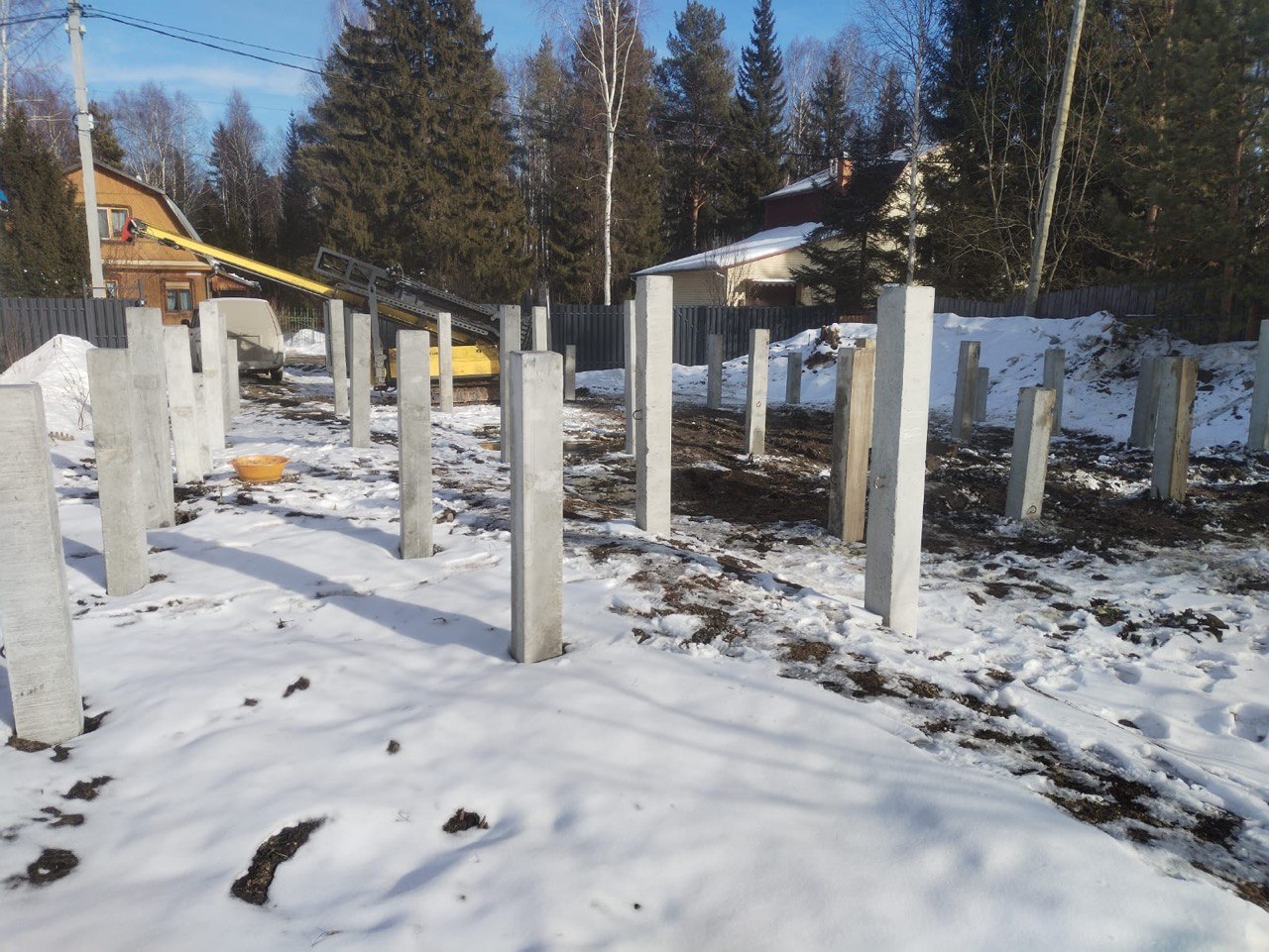 Свайное поле фундамента на ЖБ сваях: зимний монтаж, установленные железобетонные стойки на участке, подготовка под ростверк